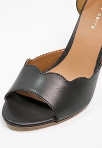 Sandale noire en cuir à bout ouvert avec un bord festonné et une doublure intérieure couleur cuir clair.