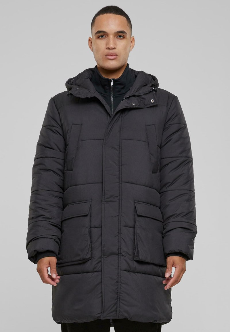 Crna podstavljena parkasta jakna s kapuljačom, koja ima dva prednja džepa i zatvaranje na zip. Materijal izgleda glatko s šivenim dijelovima za izolaciju.