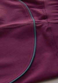 Tissu de sport bordeaux avec des coutures bleu-vert, présentant une texture lisse et des coutures plates, conçu pour le confort et la flexibilité lors des activités.