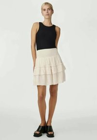 Black sleeveless top paired with a cream-colored tiered skirt with textured layers. Black chunky sandals complete the outfit.