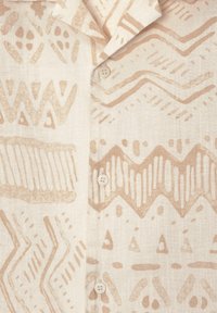 Tissu de chemise avec des motifs géométriques beiges et en zigzag sur un fond clair, comportant des boutons blancs et un col plié.