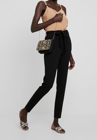 Svarta hög midja byxor med bälte detalj, beige camisole topp och sandaler med ormskinnsmönster. Mönstrad väska med silverkedjespänne.