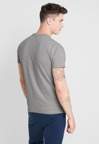 Gray short-sleeve T-shirt made of cotton, featuring a crew neck and a smooth texture, worn with navy pants.