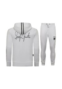 Witte hoodie en joggingbroek met zwarte strepen, met de tekst "Local Fanatic" op de achterkant en een logo met drie sterren op de broek.