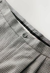 Tissu à carreaux gris avec une texture fine, plis à la taille et un détail de bouton noir sur la ceinture. Doublé d'un matériau gris lisse.