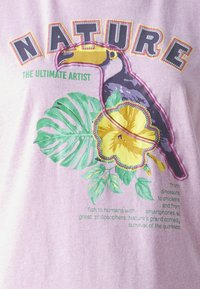 Light purple cotton t-shirt featuring a toucan, tropical leaves, and a yellow flower print with colorful text. Text reads “NATURE THE ULTIMATE ARTIST.”