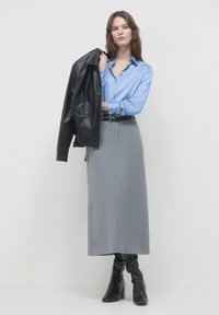 Lunga gonna grigia a righe sottili abbinata a una camicia azzurra a bottoni e una giacca di pelle nera. Stivali neri al ginocchio completano l'outfit.