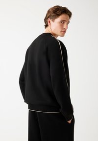 Schwarzer Sweatshirt mit strukturierter Oberfläche, ausgestattet mit einem cremefarbenen Seitenpiping und gerippten Bündchen und Saum für eine taillierte Passform.