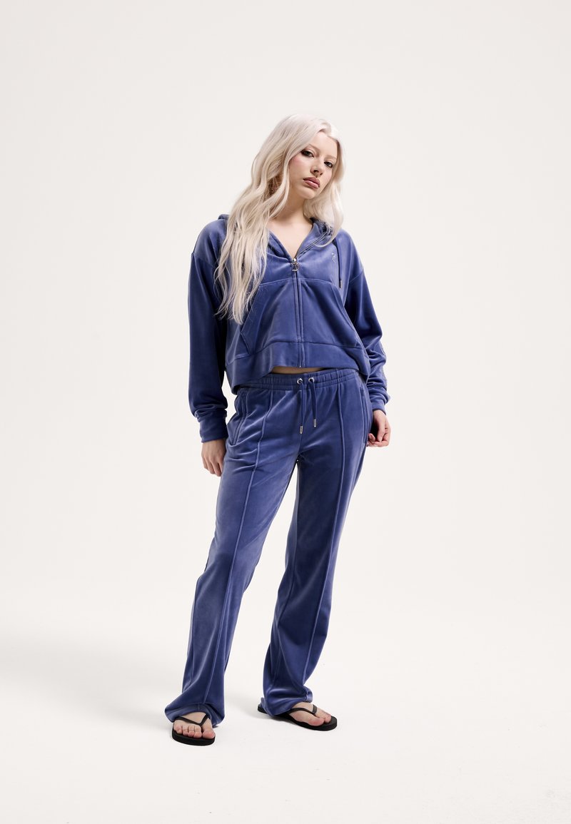 Aksamitny dres w głębokim niebieskim kolorze, z krótką bluzą na zamek i spodniami z troczkami. Gładka faktura z kontrastującymi przeszyciami.