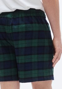 Πράσινα και ναυτικά κοντά παντελόνια με καρό σχέδιο, κατασκευασμένα από μαλακό ύφασμα, με ελαστική μέση και άνετη εφαρμογή, χωρίς ορατές τσέπες ή κλείστρα.