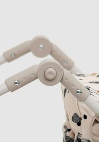 Maniglione del passeggino imbottito con impugnatura in plastica beige, struttura in metallo bianco e tessuto decorativo con motivi astratti in colori tenui.