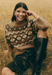 Rudas megztinis su baltomis ir juodomis geometrinėmis raštais, aukštu apykakliu. Derinamas su juoda odine sijonu ir aukštais batais.