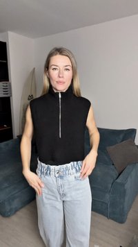 Juodas be rankovių viršus su aukštu apykakle ir priekiniais užtrauktukais, derinamas su šviesiai mėlynomis, aukštu juosmeniu džinsinėmis kelnėmis, turinčiomis susiraukšlėjusią juosmenį.