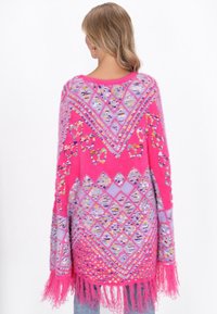 Oversized roze en lila gebreide poncho met geometrische patronen, franjes aan de onderkant en levendige kleurrijke accenten overal. Zachte, textuurrijke stof.