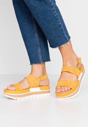 Yellow suede platform sandals with two wide straps and a buckle, featuring a chunky white sole with orange and beige accents.