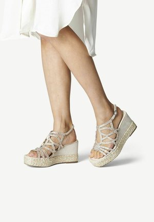 Beige wedge sandalen met kruislings gespen, versierd met rhinestones, met een gevlochten juten tussenzool en een gladde suède bovenkant.