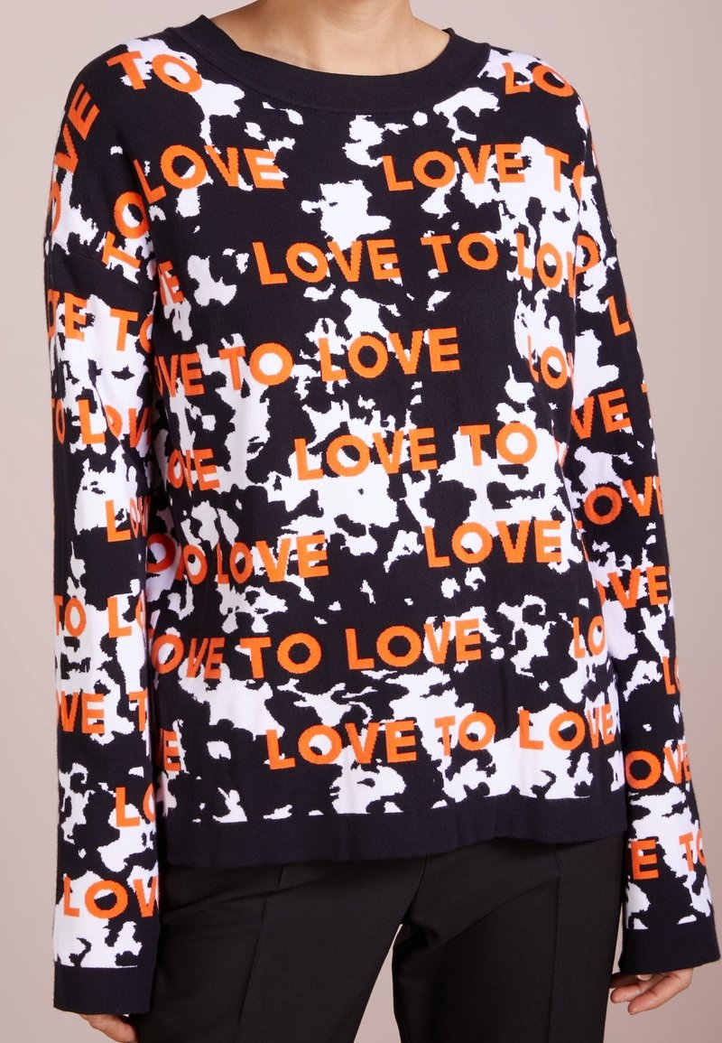 Pull noir et blanc à motifs avec le texte orange "LOVE TO LOVE" ; dispose d'un col rond et de manches longues, fabriqué en matière tricotée douce.
