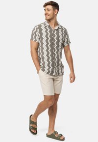 Chemise à manches courtes à motifs gris et blanc, short beige et sandales vert olive. La texture du tissu semble tissée ; la chemise a un col et des boutons.