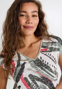 Top de manga corta con escote en V de tejido ligero, que presenta un estampado abstracto multicolor con tonos verdes, rojos y acentos dorados alrededor del cuello.