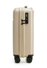 Tvrdý kufr béžové barvy s texturovaným povrchem, dvojitými zipy, kombinovaným zámkem a čtyřmi černými kolečky pro snadnou manipulaci.