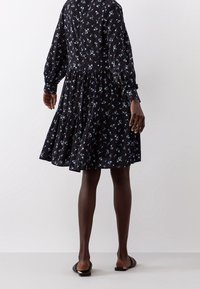 Robe noire à motifs floraux bleu clair, à manches longues et jupe à volants. Tissu doux avec une coupe décontractée et de subtils détails de manches volumineuses.