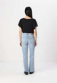 Black short-sleeve top with dotted texture paired with light blue flared jeans; features a brown brand patch at the back waist.