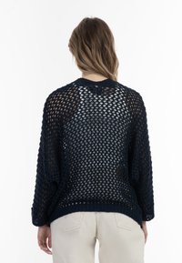 Pullover aperto blu navy con maniche lunghe e collo rotondo. Presenta una vestibilità morbida e un orlo inferiore a costine. Tessuto trasparente.
