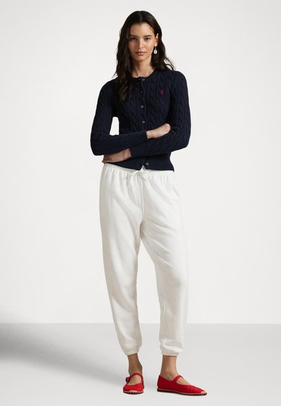 Tengerészkék kötött kardigán, fehér polárnadrág és piros lapos cipő pántos részlettel. Egyszerű, hétköznapi öltözék kontrasztos színekkel és textúrákkal.