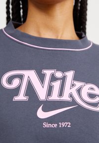 Närbild av mörkgrå skjorta med rosa Nike-logotyp, swoosh och texten "Sedan 1972" under logotypen.