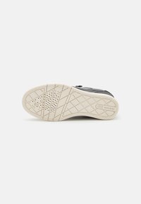 Schwarzer Sneaker mit einer strukturierten Oberseite, Gummisohle mit gemustertem Profil und einer cremefarbenen Außensohle für Grip und Haltbarkeit.