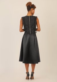 Abito nero con corpino in pizzo e maniche a scallop, gonna in satin morbido e zip sul retro nascosta. Indossato con tacchi neri.