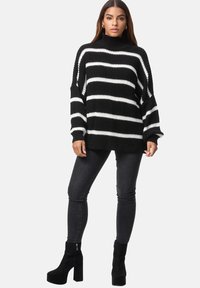 Maglione a righe bianche e nere in maglia con collo alto e maniche larghe, abbinato a jeans neri aderenti e stivali alla caviglia con piattaforma.