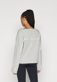 Ανοιχτό γκρι φούτερ με χαλαρή εφαρμογή, πτώση μανικιών, άγρια ραφή και φαρδύ λαιμό, συνδυασμένο με μαύρα κολάν.