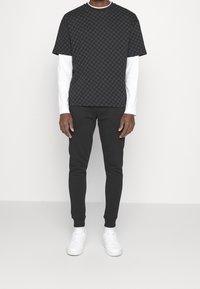 Černé tričko s potiskem vrstvené přes bílé dlouhé rukávy, doplněné černými zúženými kalhotami a bílými teniskami. Hladká tkanina, ležérní střih.