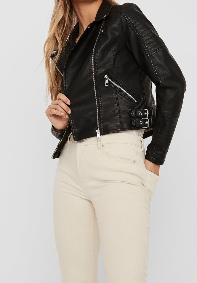 Giubbotto di pelle nera con dettagli trapuntati sulle spalle, chiusura con zip asimmetrica e hardware argentato, abbinato a jeans fitted beige chiaro.