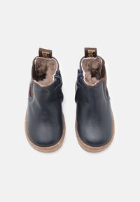 Botas de tobillo de cuero azul marino con un suave forro de piel marrón, costuras expuestas y una suela marrón texturizada. Presentan un zipper lateral y una pestaña de agarre.