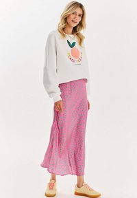 Biely sveter s nápisom "PEACH PLEASE" a grafickým znázornením broskyne, kombinovaný s ružovou sukňou s bodkami. Svetlé tenisky dotvárajú celý outfit.
