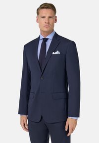 Temno modra čaka z eno gumbom, zarezanim ovratnikom, dvojno sprednje žepke in teksturirano tkanino. Srajca ima svetlo karo vzorec.