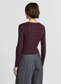 Bordeauxroter, gerippter Strickpullover mit langen Ärmeln, rundem Ausschnitt und figurbetonter Silhouette, kombiniert mit strukturierten, grauen, hoch taillierten Hosen.