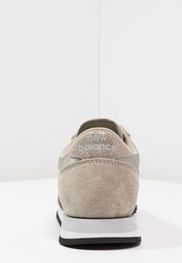 Šedé semišové tenisky s síťovinovými detaily, s černou gumovou podešví a logem "new balance" v světle šedé barvě na patě.