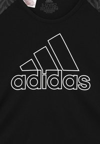 Svart atletisk t-shirt med en stor vit Adidas-logotyp med tre diagonala ränder, gjord av stretchigt material med en mjuk textur.