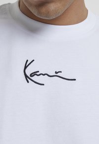 Hvit bomull t-skjorte med svart brodert tekstdesign. Rund halslinning og korte ermer. Myk tekstur med minimalistisk stil.