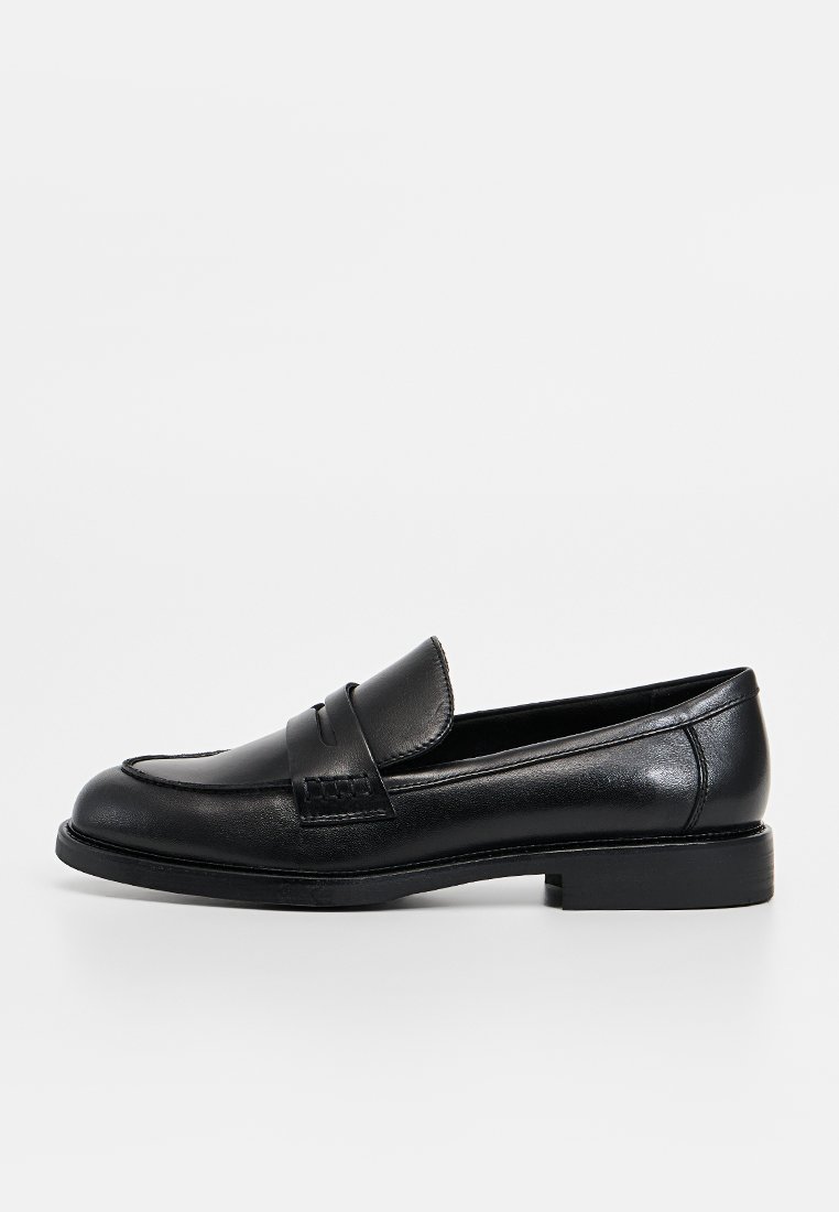 Mocassin en cuir noir avec un bandeau cousu à l'avant, talon plat et texture lisse. Présente une forme classique et un design minimaliste.
