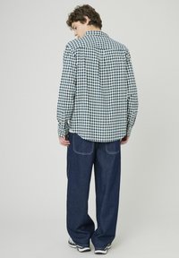 Chemise à carreaux bleu marine et blanche, en tissu coton, avec des poignets boutonnés, associée à un pantalon en denim bleu foncé ample. Détails et coutures visibles au dos.