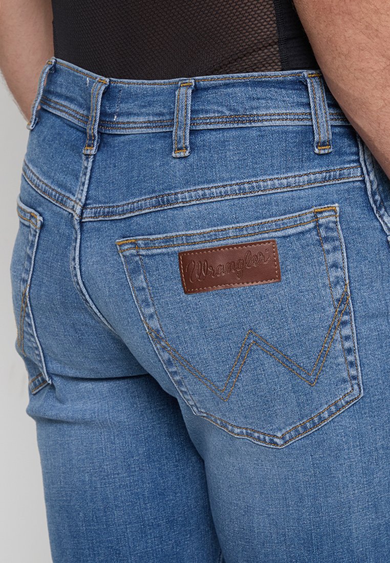 Zbliżenie na ty�ł niebieskich dżinsów z brązową skórzaną metką Wrangler oraz przeszytymi kieszeniami z charakterystycznym wzorem litery W.
