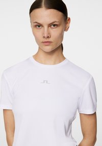 Vit kortärmad tränings T-shirt med rund halsringning och silverfärgad logotyp på bröstet. Slät tygkvalitet med en kroppsnära design.