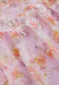Tissu rose clair transparent avec motif floral. Présente des accents à volants et une texture douce. Matériau délicat et léger avec des nuances pastel.