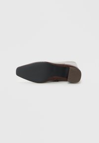 Chaussure marron avec un dessus en cuir texturé, bout pointu et un petit talon. La semelle est noire et plate avec une finition lisse.