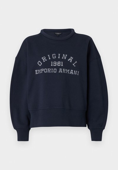 Μπλε σκούρο φούτερ με ριμπ άκρα μανσετών και τελειώματος, με λευκό κεντημένο κείμενο "ORIGINAL 1981 EMPORIO ARMANI" στο στήθος.