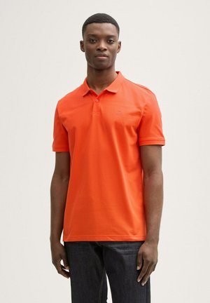 Polo shirt lengan pendek dari katun oranye cerah. Dilengkapi dengan kerah lipat, placket dua kancing, dan logo kecil di dada kiri.